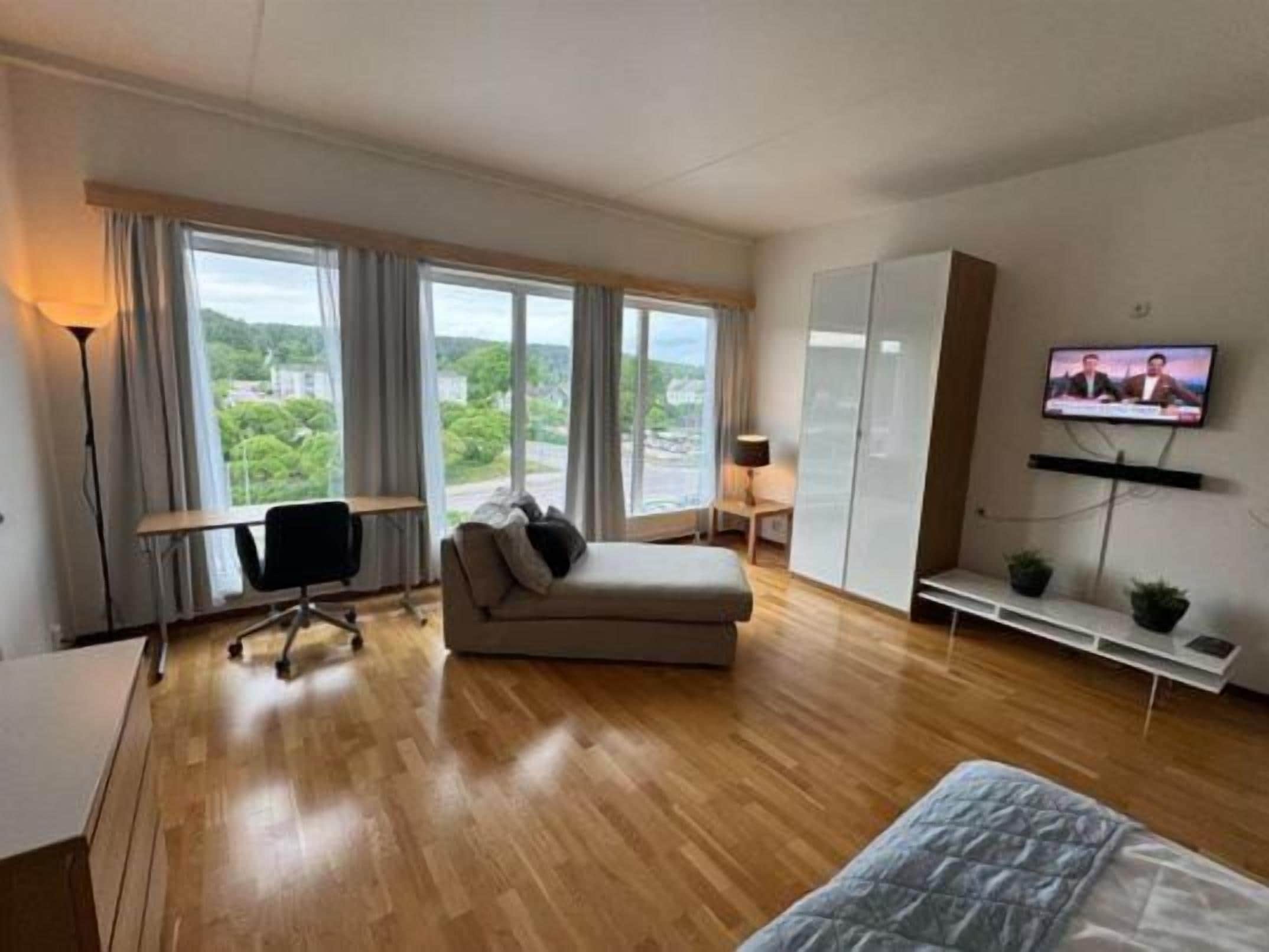 Une chambre d’hôtel moderne avec un plancher en bois, un canapé, un bureau, une télévision et une vue sur l’extérieur.