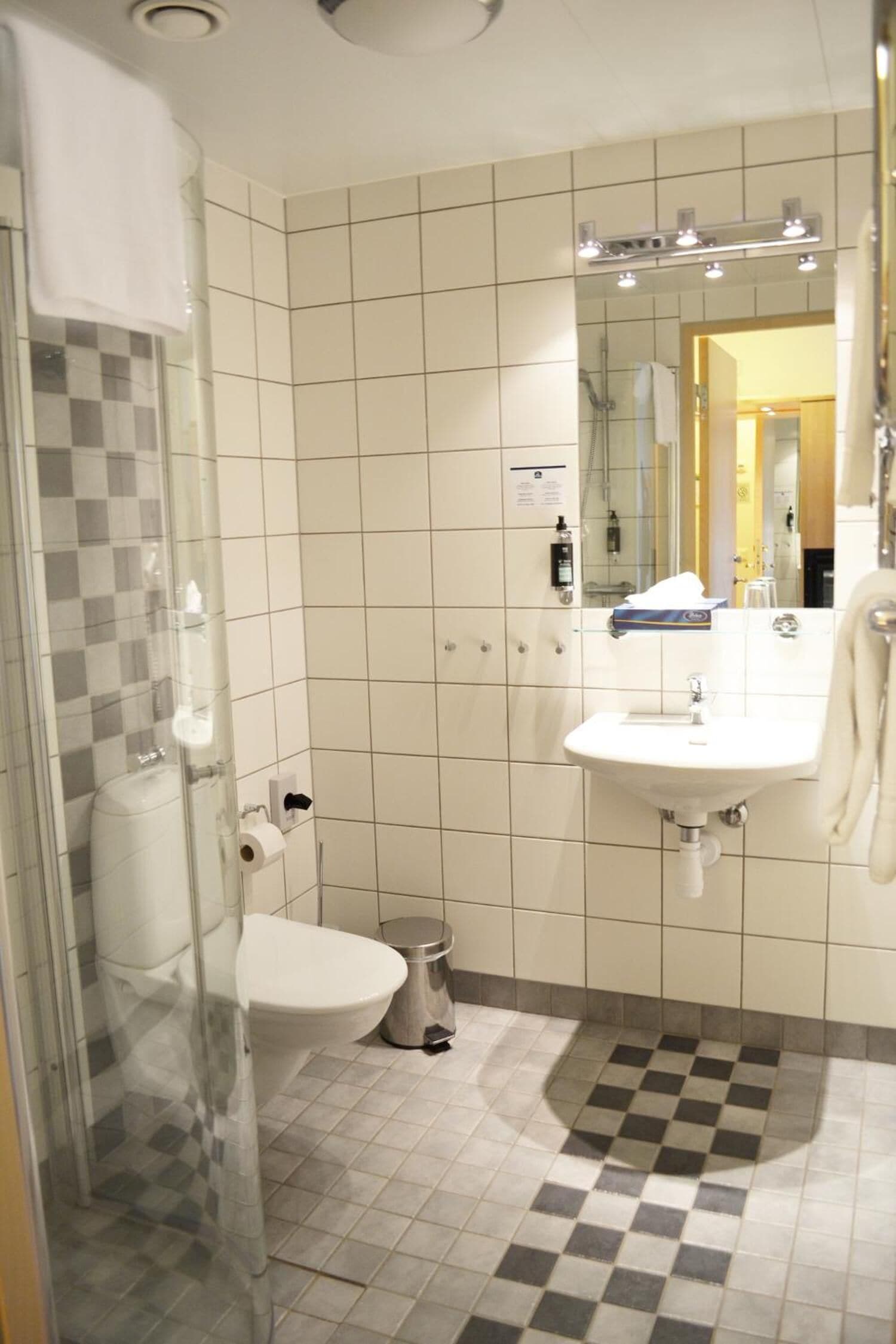 A bathroom with a glass shower enclosure, a white sink, and a tiled floor.