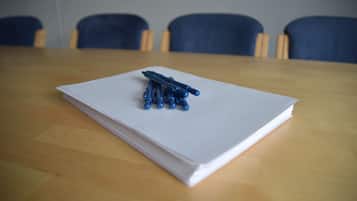 A stack of white papers on a wooden table with blue pens arranged on top.
