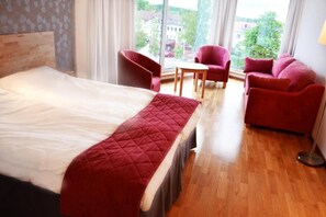 Relax in this inviting space with a large bed, comfortable seating, and a window offering views of the surrounding buildings and trees.