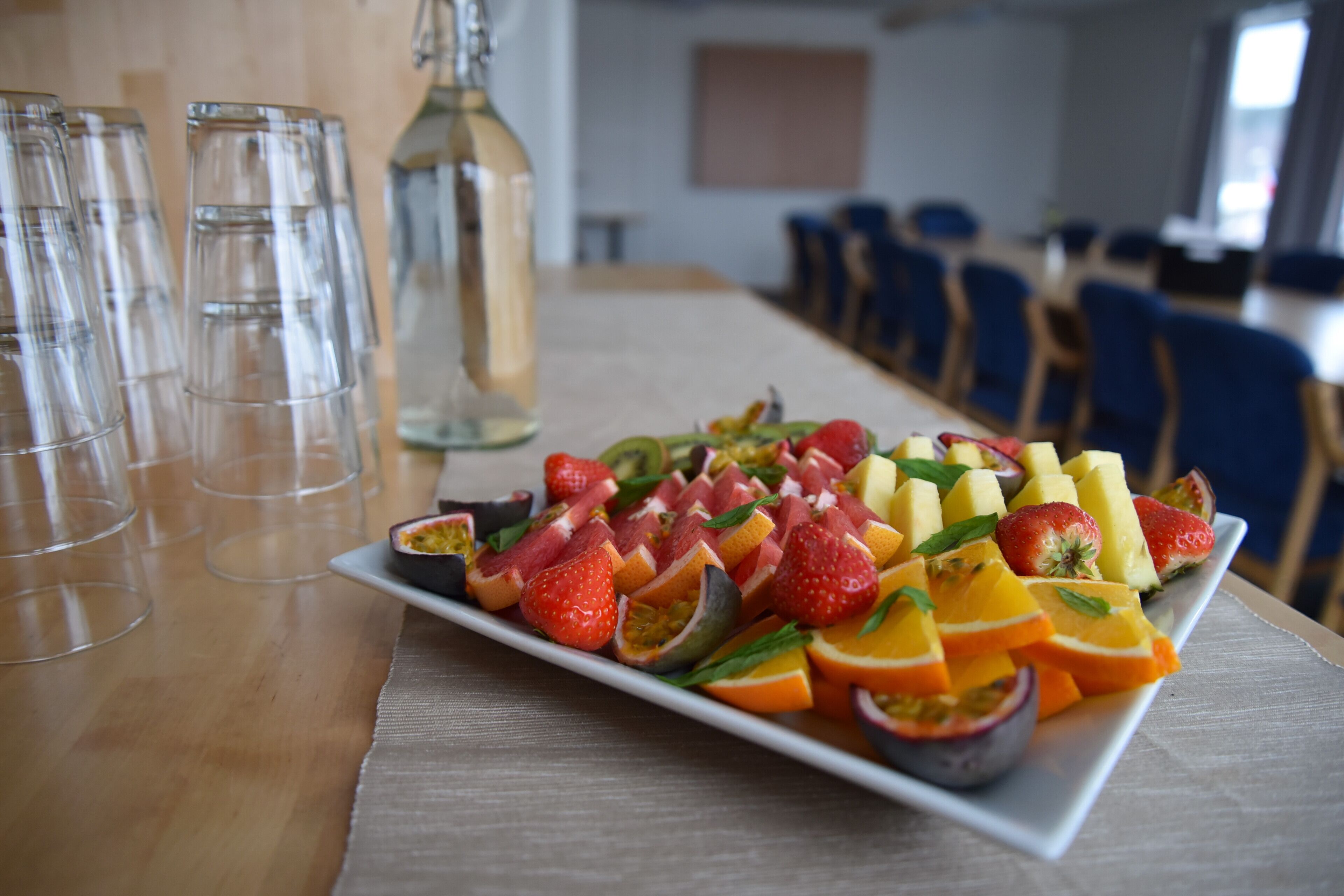 A fruit platter on a table with empty glasses and a bottle of water.