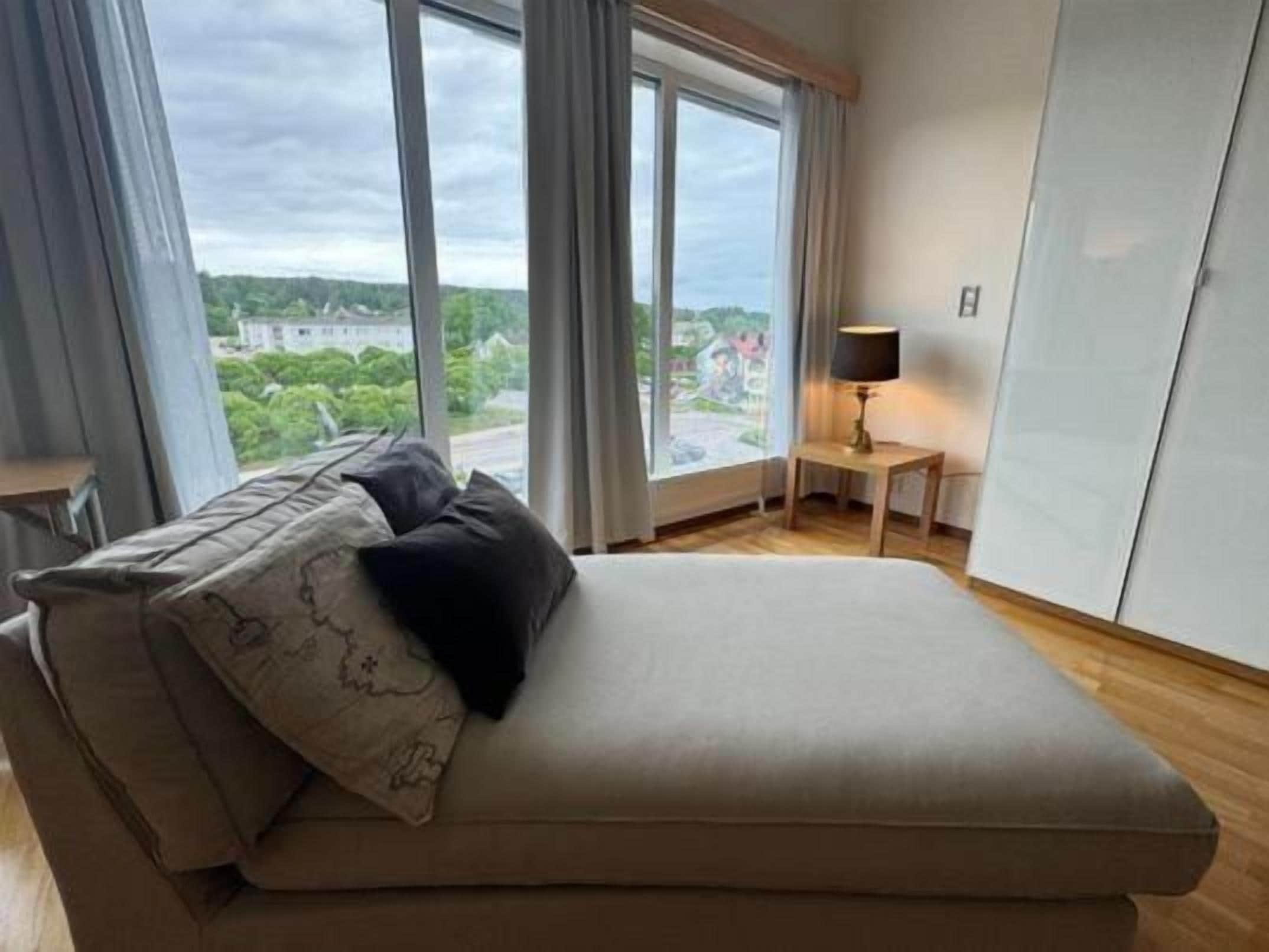 A bedroom with a bed, a nightstand, a lamp, and a view of the outdoors.
