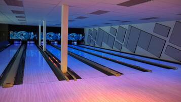 Een bowlinghal met meerdere banen, verlicht door overheadlampen, en een kleurrijke vloer.