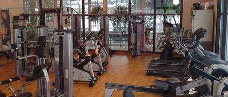 Un gimnasio con máquinas de cardio, pesas y vistas a un cuerpo de agua a través de amplias ventanas.