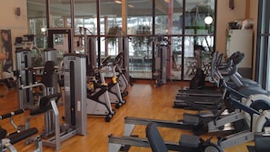 A gym with cardio machines, weight machines, and a view of a body of water through large windows. - Hotell Årjäng (Årjäng)