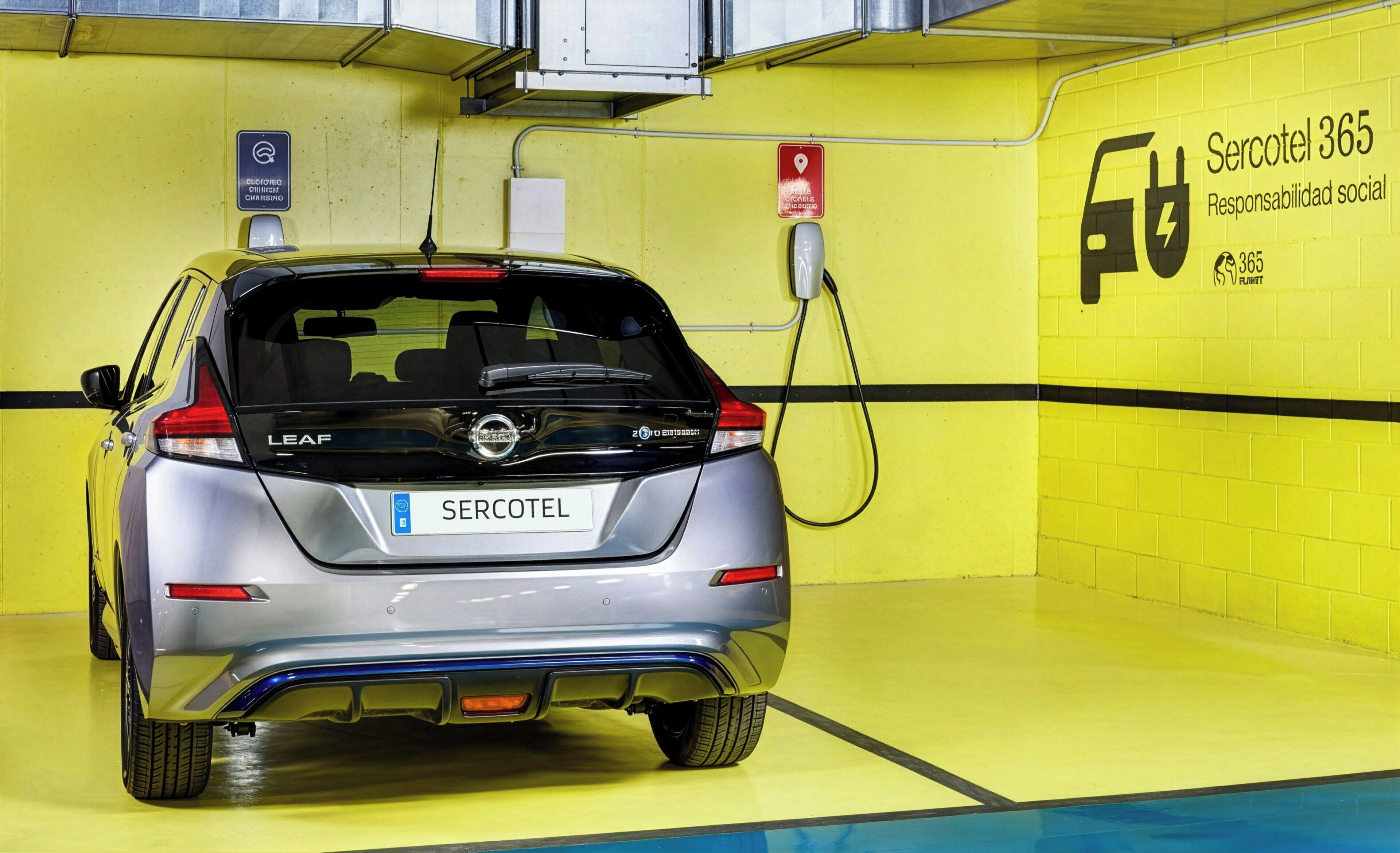 Un coche eléctrico LEAF plateado cargándose en una estación, dentro de un área de estacionamiento con paredes amarillas y un cartel que dice 'Sercotel 365 Responsabilidad social'.