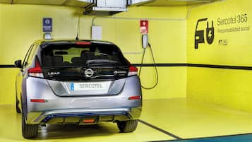 Un coche eléctrico LEAF plateado cargándose en una estación, dentro de un área de estacionamiento con paredes amarillas y un cartel que dice 'Sercotel 365 Responsabilidad social'.