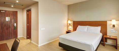 Ein Hotelzimmer mit einem großen Bett, einem Holzkopfende, Nachttischlampen, einem Nachttisch aus Holz und einem Schreibtisch mit Stuhl.