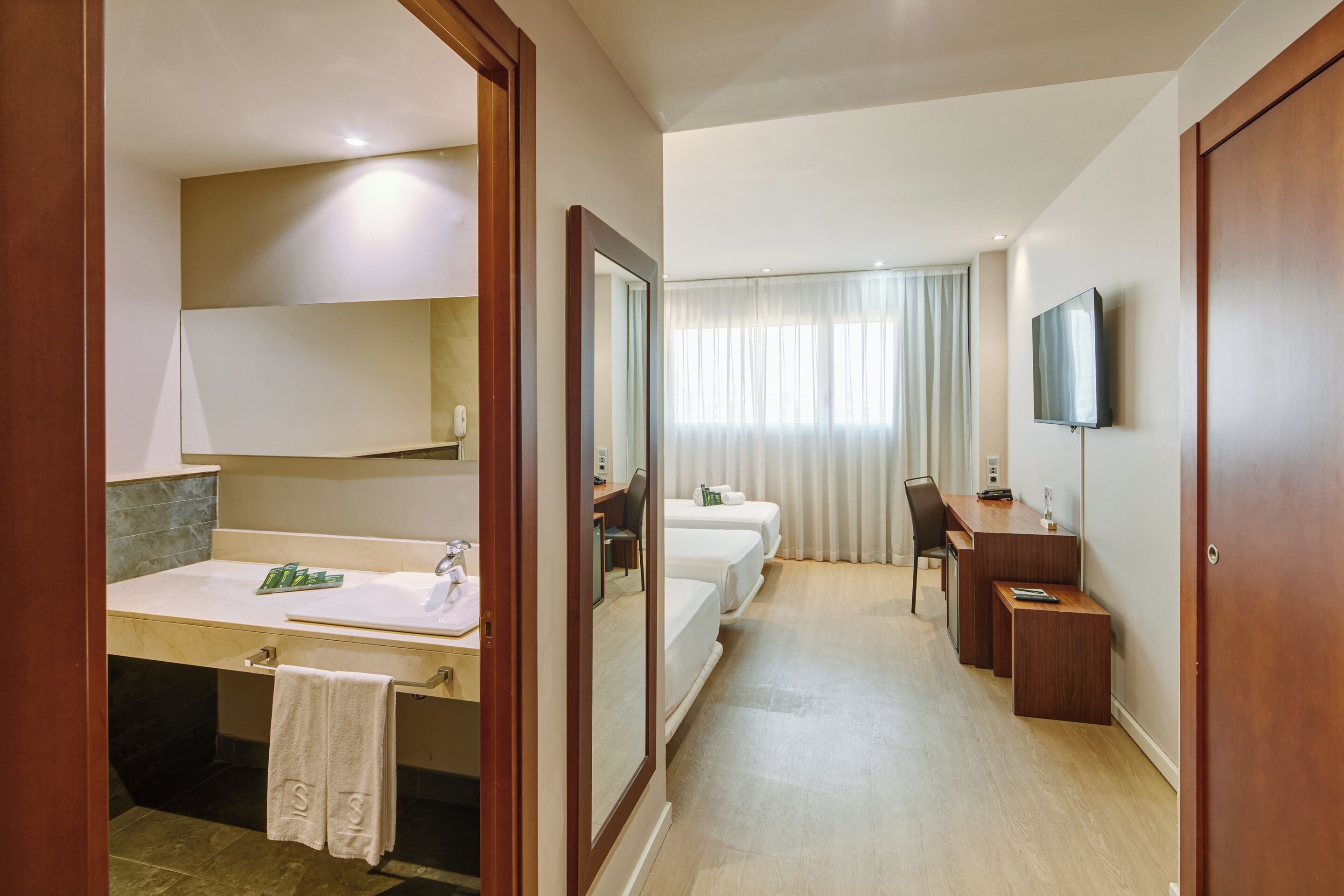 Una habitación de hotel con baño, cama, escritorio y televisión.
