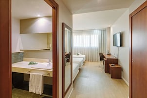 Una habitación de hotel con baño, cama, escritorio y televisión.
