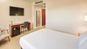 A hotel room with a bed, a desk with a chair, a television, a mirror, and a door.