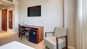 A hotel room with a wooden desk, a chair, a flat-screen TV mounted on the wall, and a small refrigerator. - Hotel Sercotel Ciutat de Montcada (Montcada I Reixac)