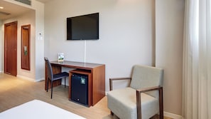 Hotellihuoneessa on puinen työpöytä, tuoli, seinälle asennettu taulutelevisio ja pieni jääkaappi.