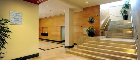 A hotel lobby with a marble floor, a staircase, and a sign listing room types.