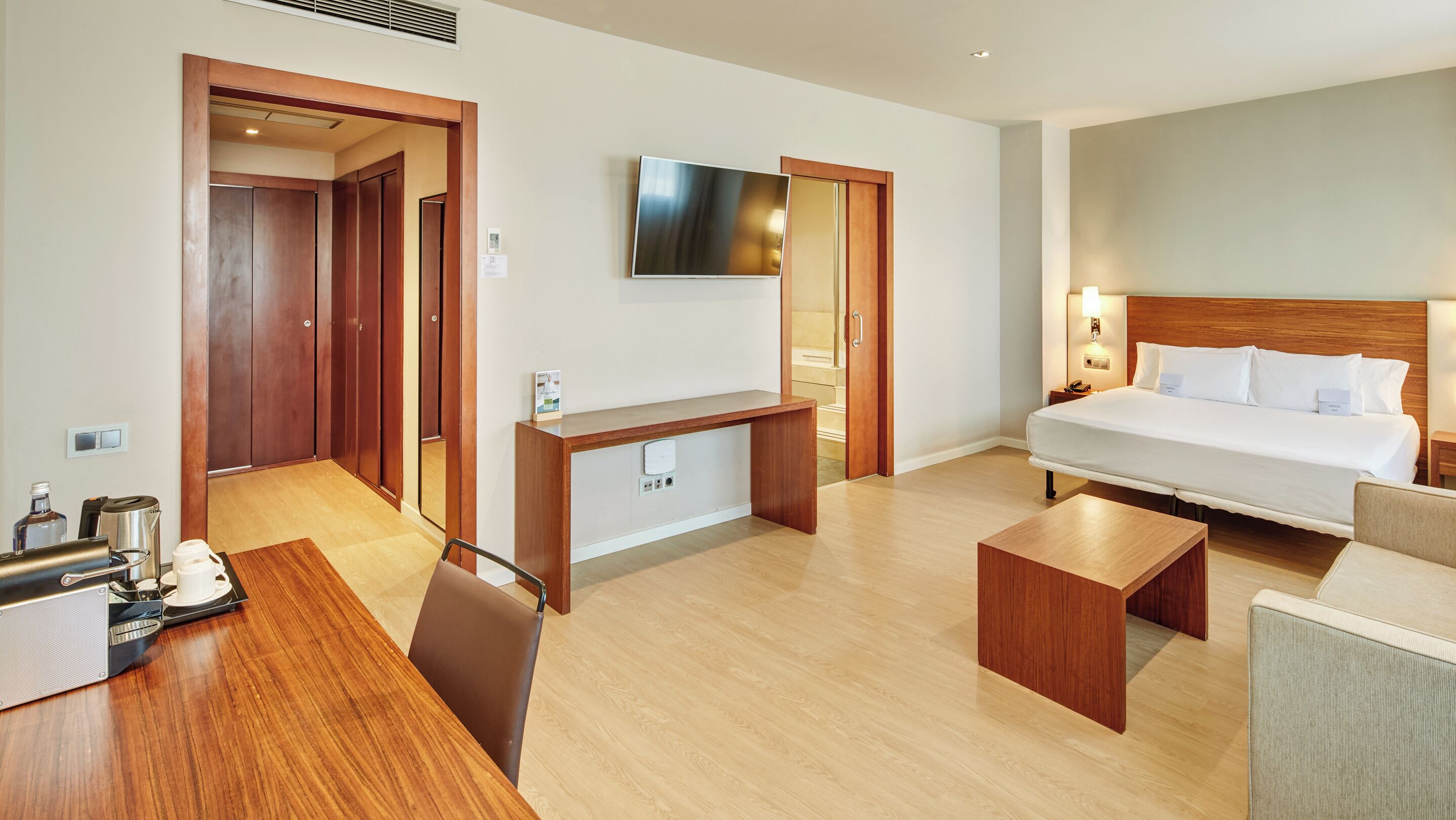 A hotel room with a bed, desk, chair, and a TV on the wall.