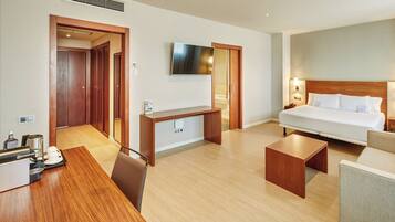 A hotel room with a bed, desk, chair, and a TV on the wall.