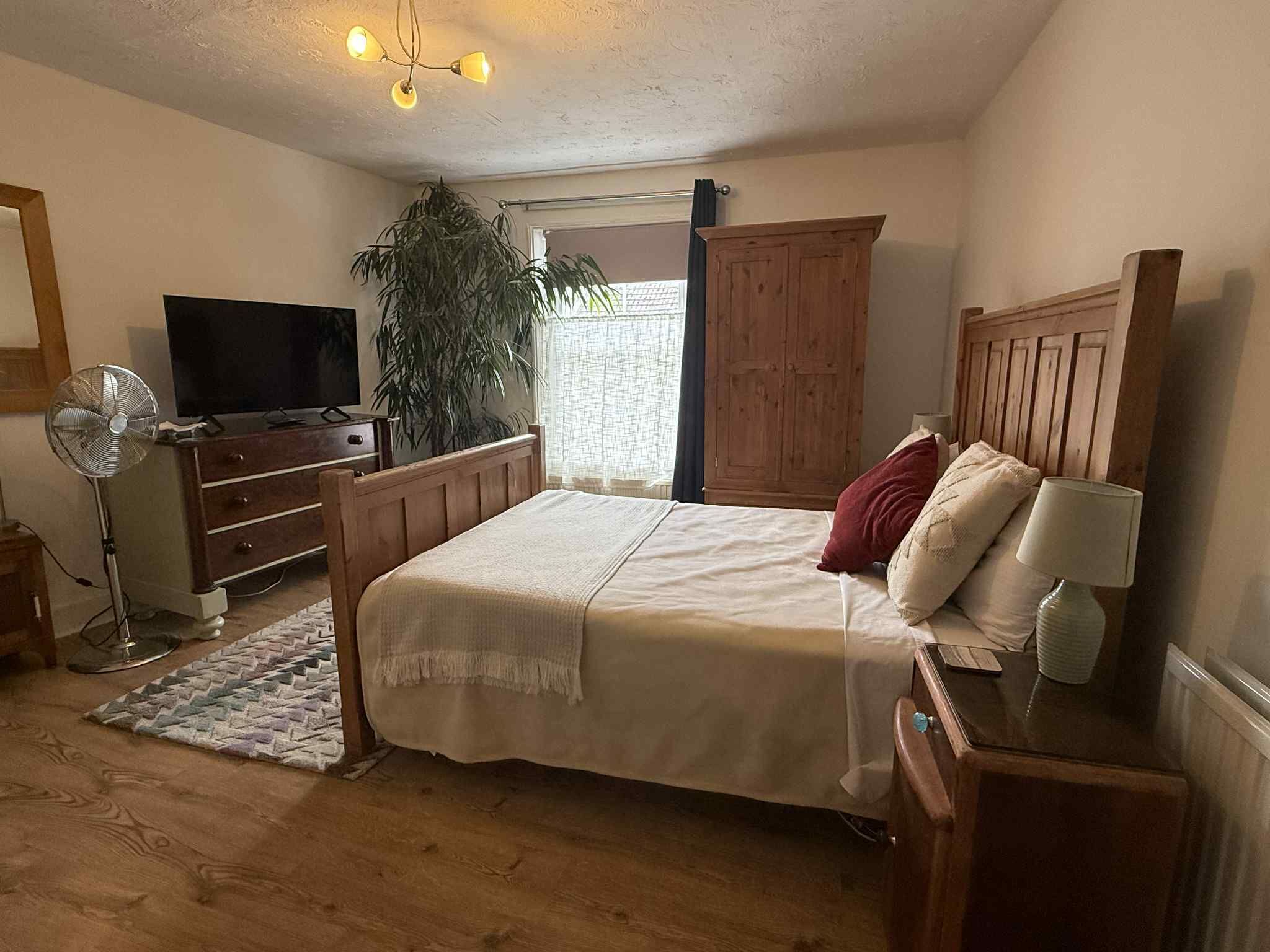 Un dormitorio con cama, cómoda, televisor, ventilador y ventana con cortinas.
