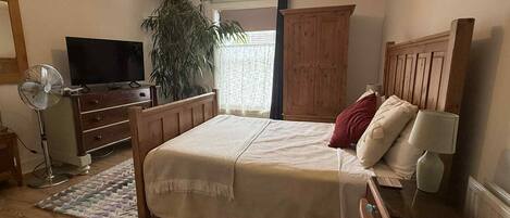 Un dormitorio con cama, cómoda, televisor, ventilador y ventana con cortinas.