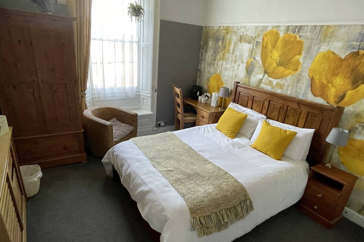 Un dormitorio con una cama grande, una mesita de noche de madera, un escritorio, una silla y una ventana con cortinas.