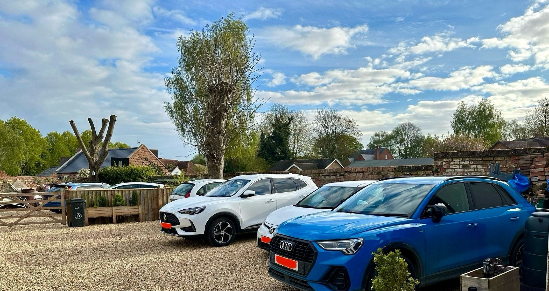 A parking area with several cars, including a blue Audi and a white Volkswagen, under CCTV protection.