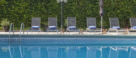 A swimming pool with lounge chairs and umbrellas, surrounded by a hedge.