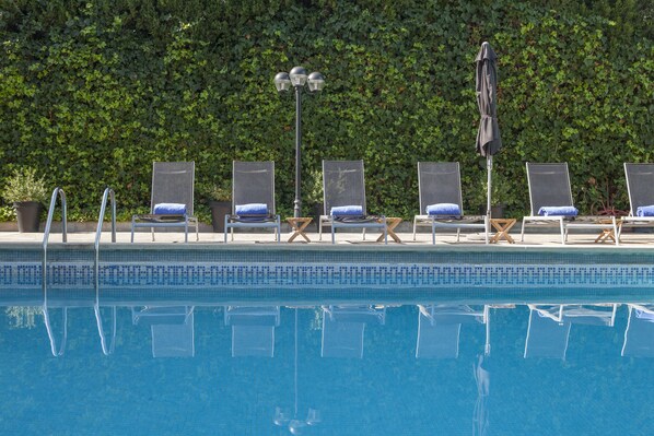 A swimming pool with lounge chairs and umbrellas, surrounded by a hedge.