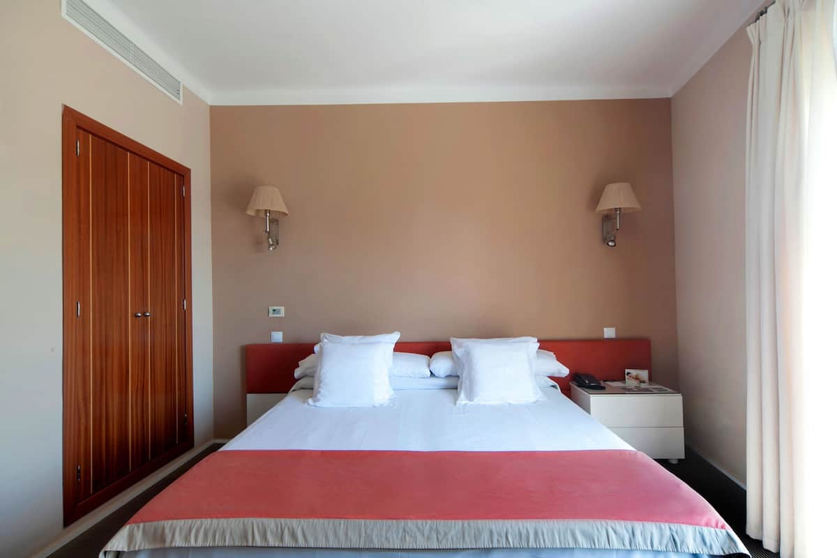 Ein Hotelzimmer mit einem großen Bett, zwei Nachttischlampen, einem Nachttisch und einem Kleiderschrank.