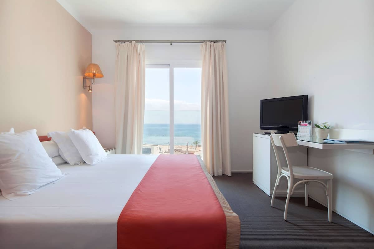 Ein Hotelzimmer mit Bett, Schreibtisch, Fernseher, Sessel und Meerblick.