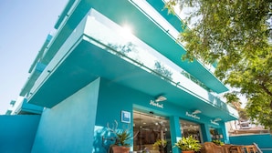 Un hotel con fachada azul, entrada visible y terraza.