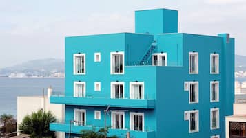 Un edificio moderno azul con múltiples ventanas y balcones, que da vistas a una masa de agua y montañas distantes.