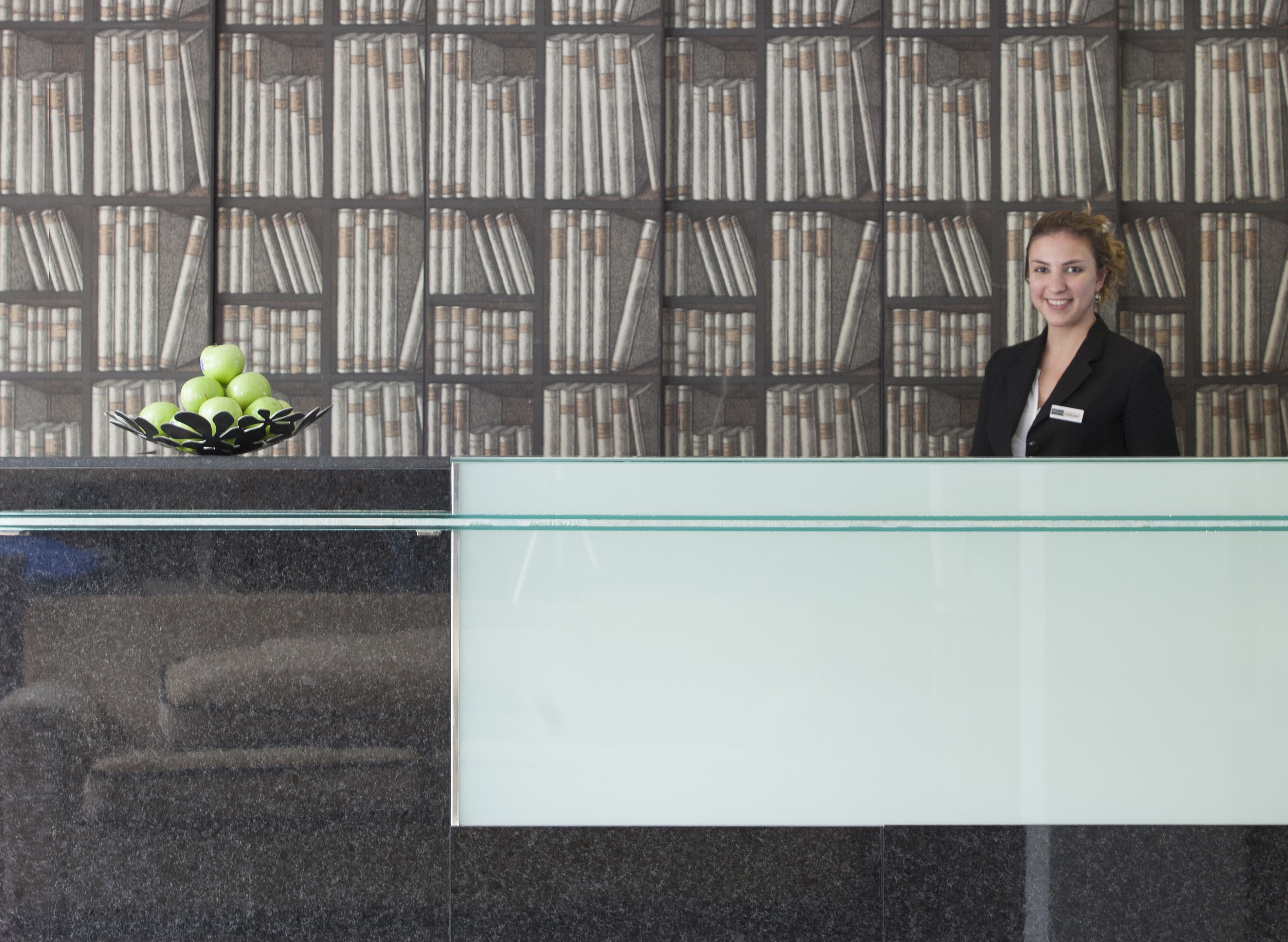 A reception desk with a glass partition, a nameplate, and a bowl of green apples.