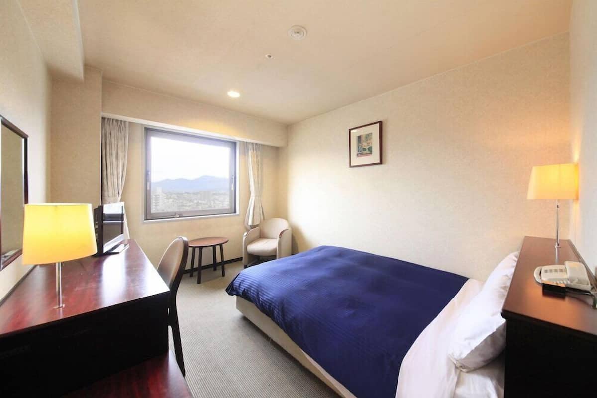 Een hotelkamer met een bed, een bureau, een stoel, een raam met uitzicht en een lamp.