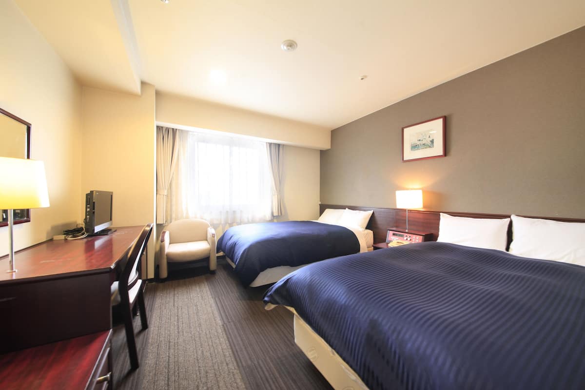 Een hotelkamer met twee bedden, een bureau, een stoel en een raam met gordijnen.
