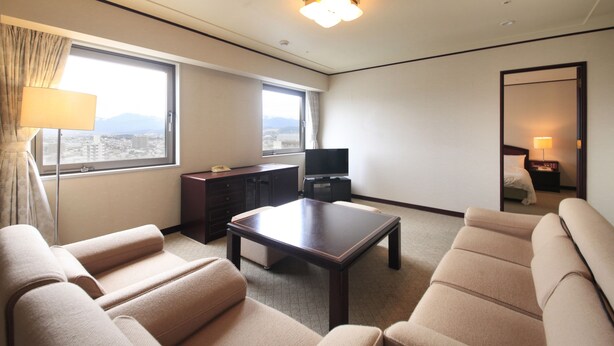 A hotel room with a large window, a flat-screen TV, a sofa, a coffee table, and a mirror.