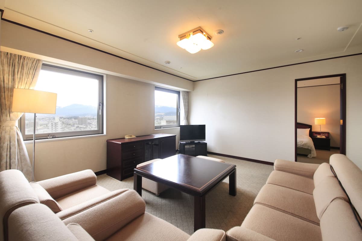 Een hotelkamer met een groot raam, een flatscreen-tv, een bank, een salontafel en een spiegel.
