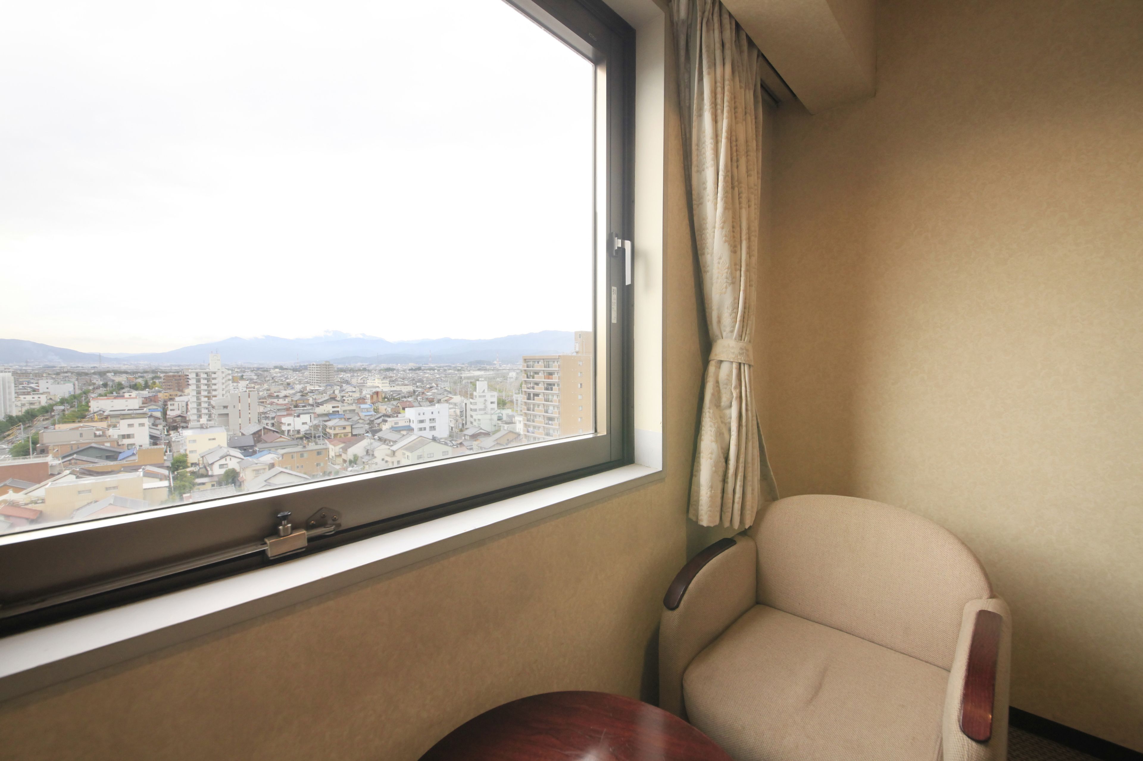 A room with a large window offering a city view, a chair, and a small table.