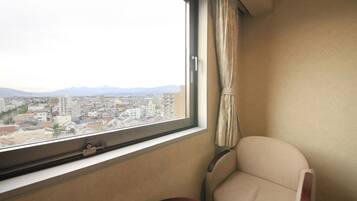 A room with a large window offering a city view, a chair, and a small table.