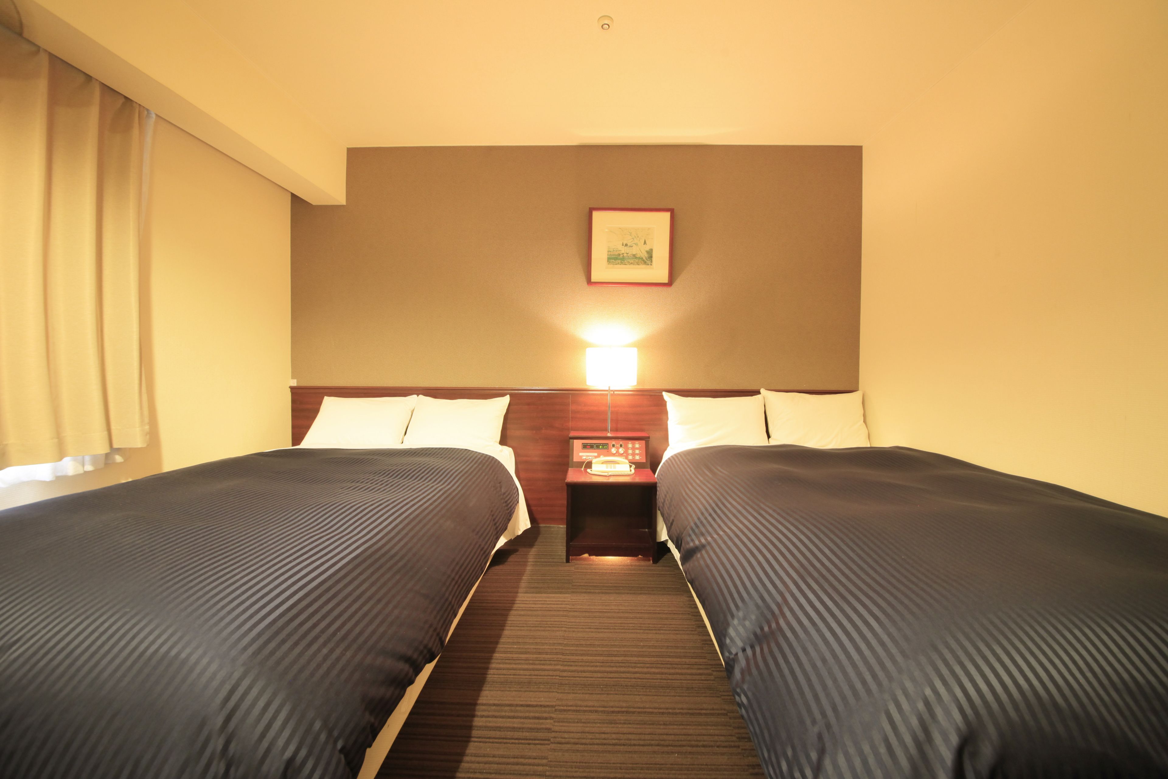 Una habitación de hotel con dos camas, una mesita de noche con una lámpara y un cuadro en la pared.