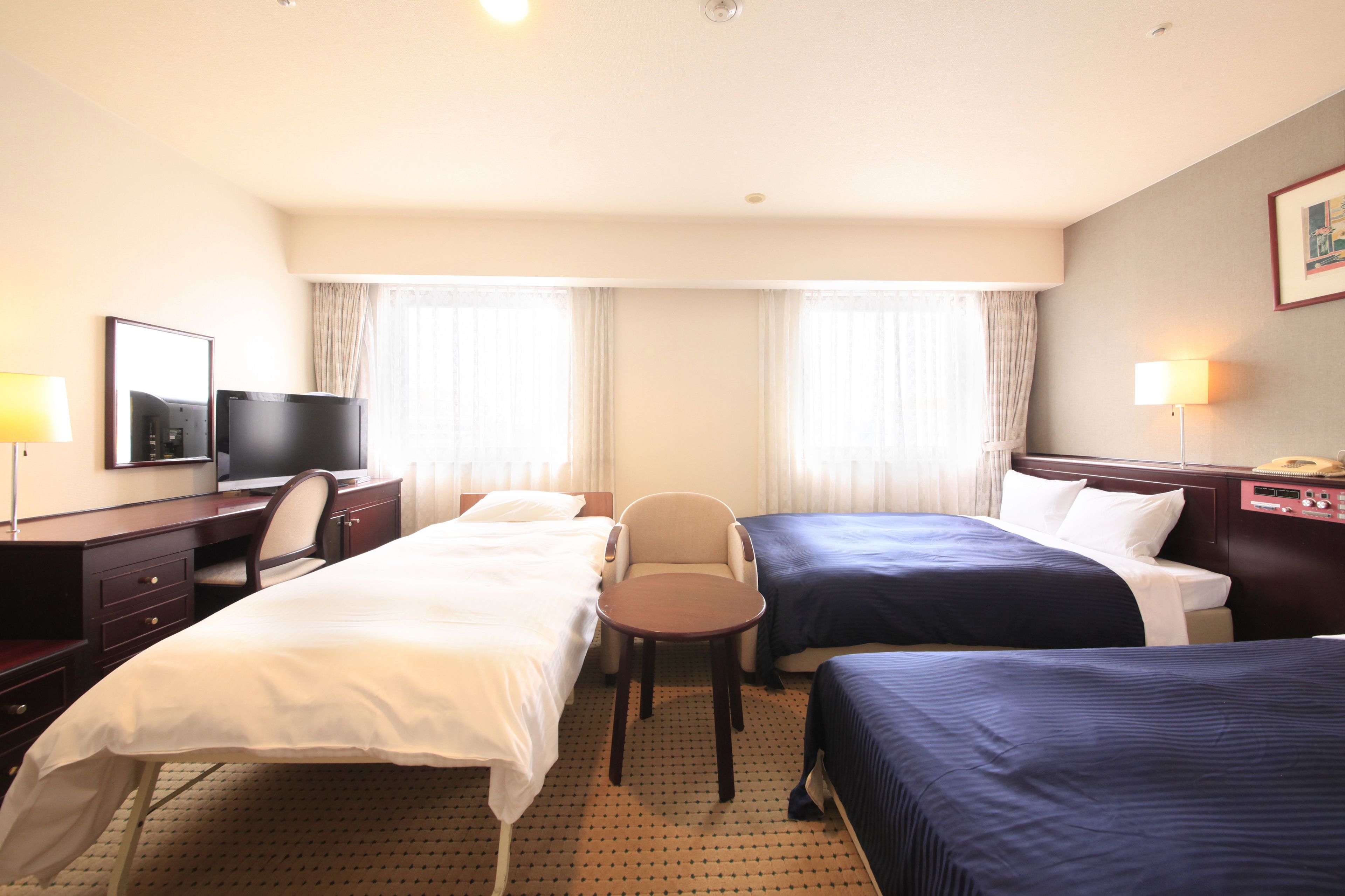 Quarto de hotel com duas camas, uma escrivaninha com televisão, uma cadeira e um abajur.