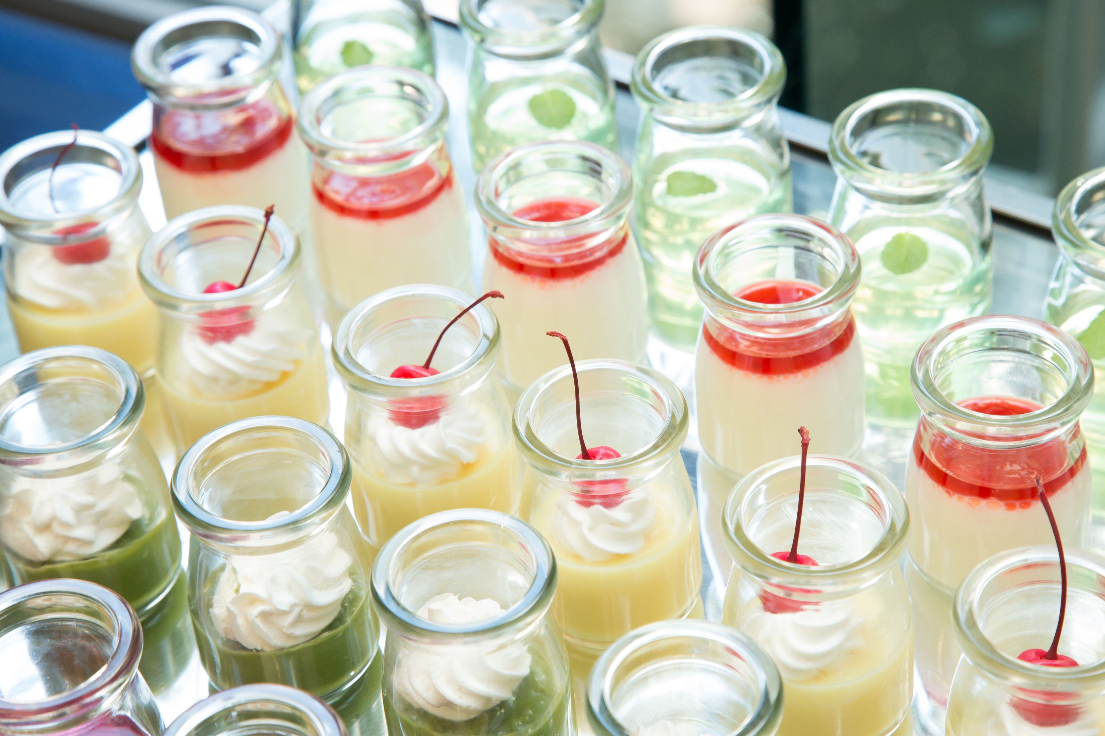 A variety of desserts in small glass jars, each topped with whipped cream and a cherry.