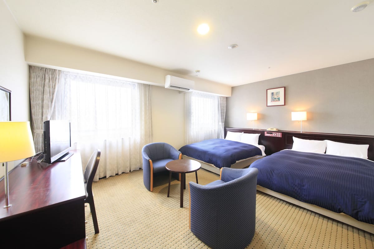 Een hotelkamer met twee bedden, een bureau, een stoel, een klein tafeltje en een lamp.