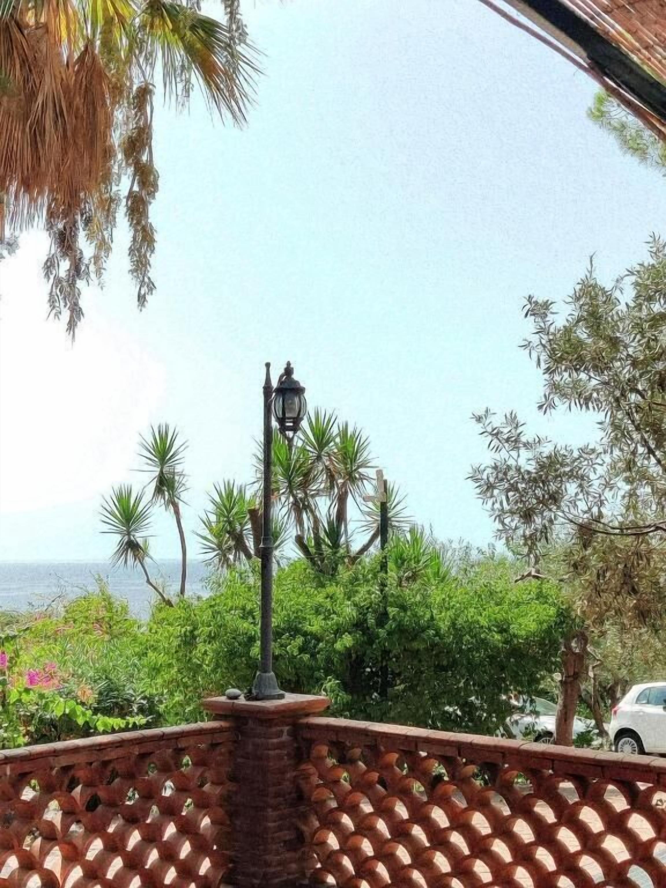 Un balcón con piso de baldosas, un farol y vistas al mar y la vegetación.