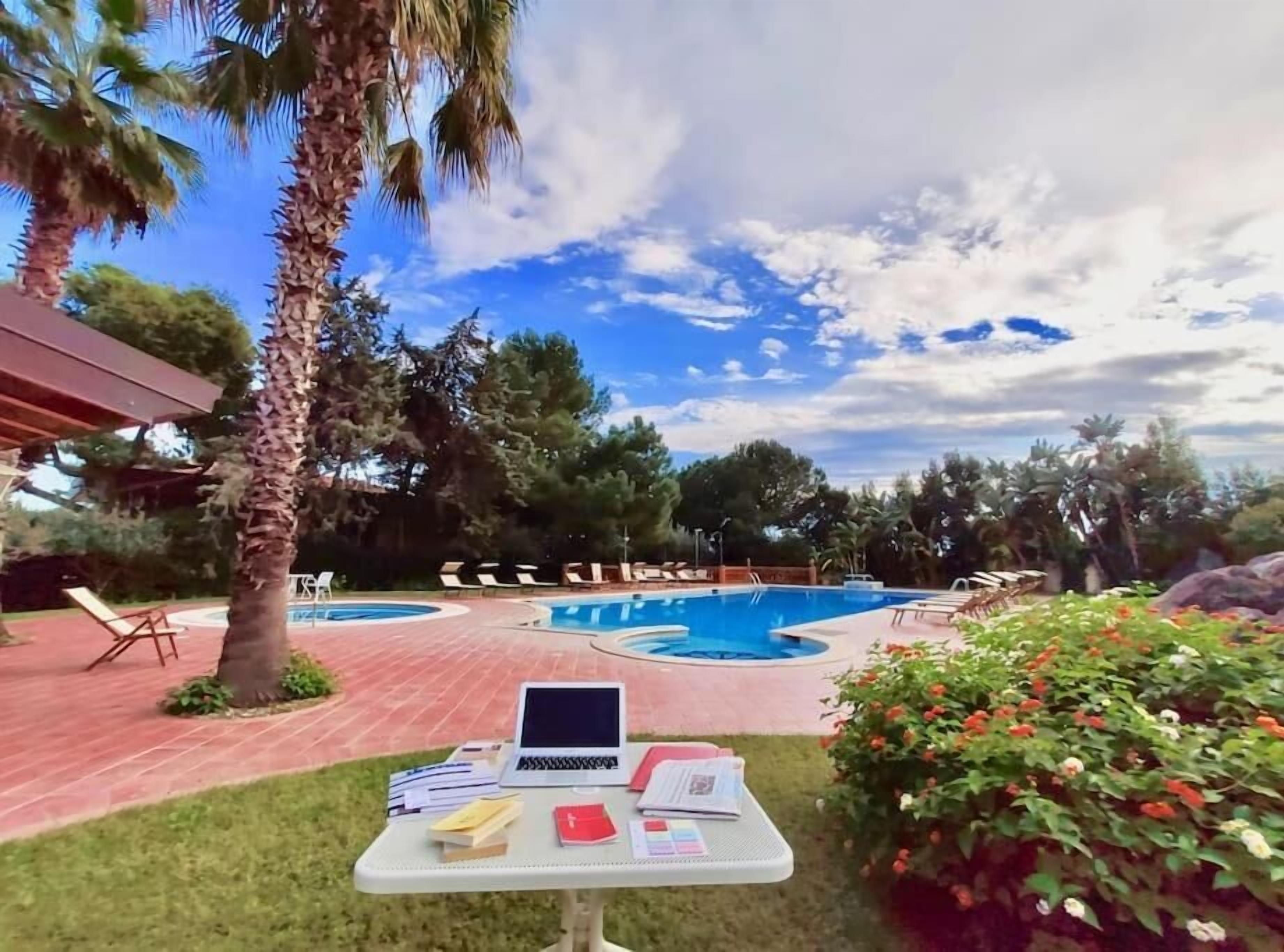 A pool area with lounge chairs, a laptop on a table, and a clear sky.