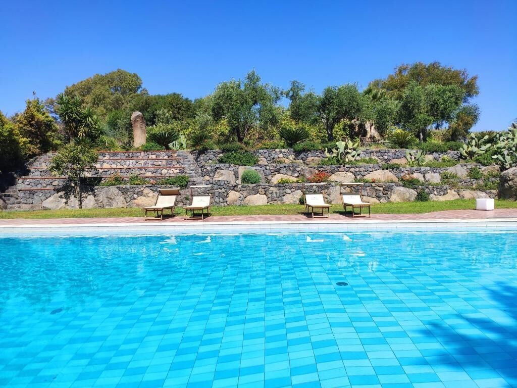 Una piscina con muro de piedra y sillas de descanso.