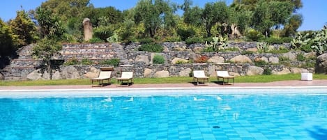 A swimming pool with a stone wall and lounge chairs.