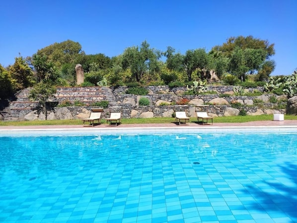 Una piscina con muro de piedra y sillas de descanso.