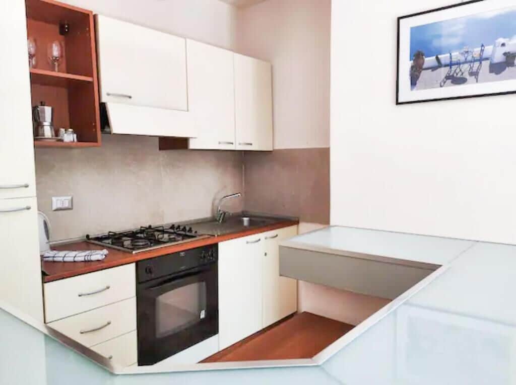 Une cuisine de taille réduite avec des meubles blancs, une cuisinière à gaz et un évier.