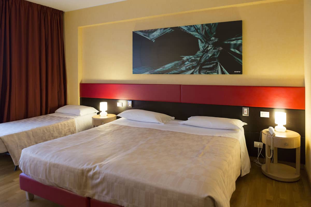 A hotel room with two beds, a red headboard, a wall-mounted artwork, bedside lamps, and a bedside telephone.