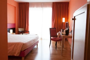 A hotel room with a bed, a desk with a computer, a chair, and a window with curtains.