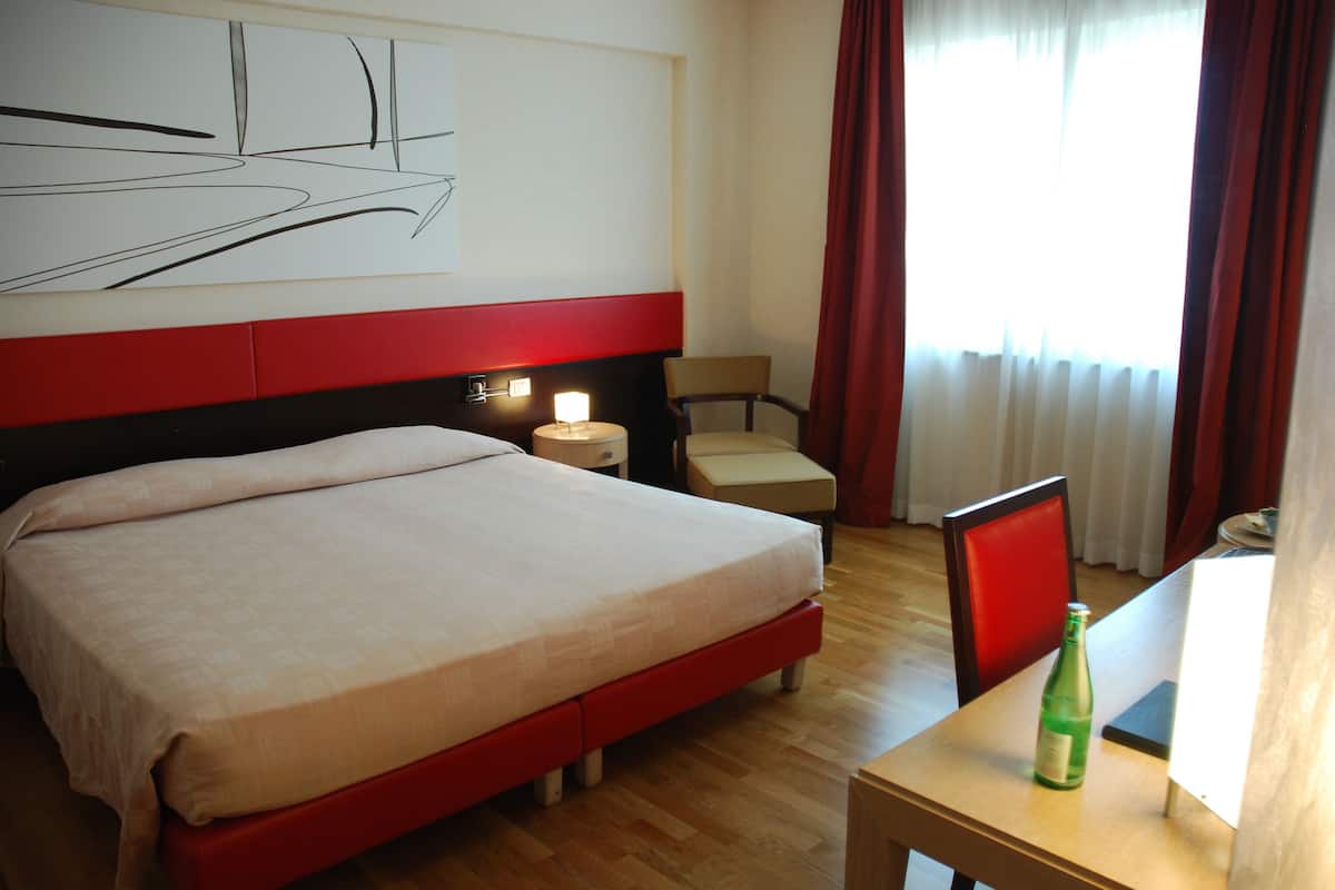 A hotel room with a large bed, a desk, a chair, and a window with curtains.